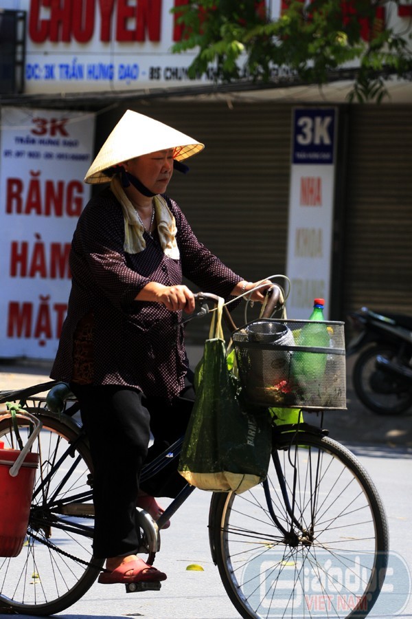 Một bà cụ bán trà đá với chiếc khăn mặt vắt vai để thấm mồ hôi và chiếc nón rộng vành